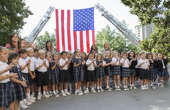 Christ the King School first graders and teachers applaud the public safety officials and first responders as they enter the Cathedral of Christ the King for the Blue Mass. In the background is an American flag, 20 feet by 30 feet, held up by two Atlanta Fire Rescue Department ladder trucks. Photo By Michael Alexander