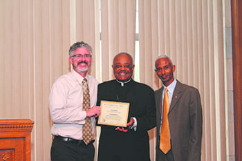 Staff reporter Andrew Nelson, left, and staff photographer Michael Alexander, right, were presented with an award from the Catholic Press Association for their work on Georgia Bulletin articles. Archbishop Wilton D. Gregory was on hand to present the awards at a reception following a Mass for the Catholic media.
