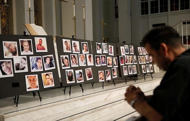 A man prays June 15 in front of photographs of victims of the mass shooting at the Pulse nightclub in Orlando, Fla., during a vigil at a church in Orlando. CNS photo/Jim Young, Reuters