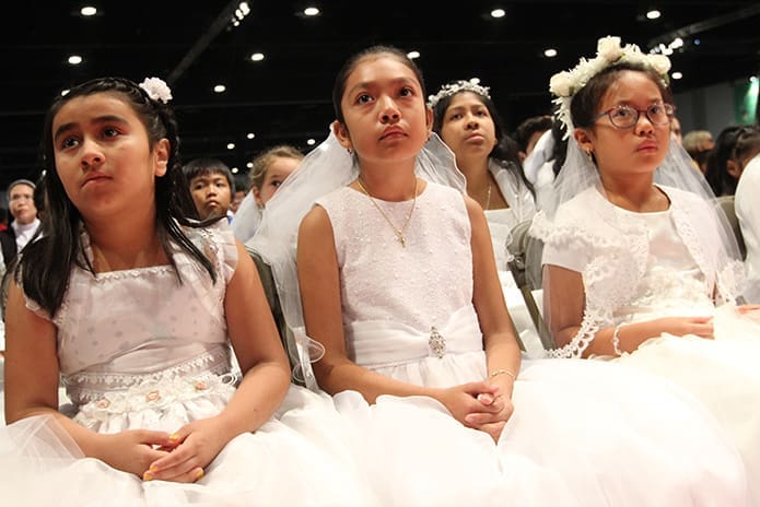 (L-r) Dressed in their first holy Communion dresses, (l-r) Heidy Juarez and Helen Ramirez of St. Paul of the Cross Church, Atlanta, and Allison Nguyen of St. Monica Church, Duluth, listen to a ure reading from the front row during the Benediction service. Photo By Michael Alexander
