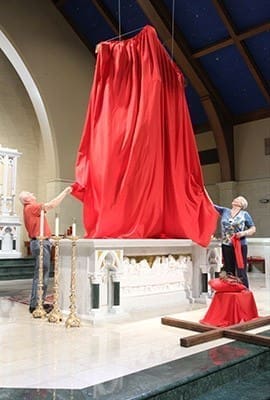 St. Peter Chanel Church facilities support Dave Petit, left, and event coordinator Doni Strok remove the red cover from the crucifix. Photo By Michael Alexander
